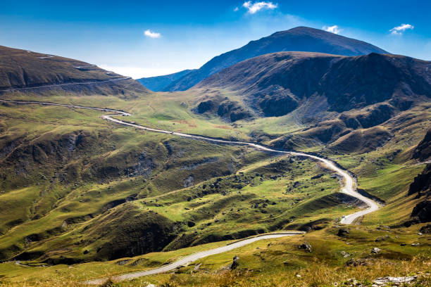 Mountain Landscape with Winding Road Wide angle color image depicting a scene in the stunning Carpathian mountains of Romania. A winding road twists and turns through the dramatic mountainous landscape, which is offset by a dazzling blue sky and cloudscape. Room for copy space. carpathian mountain range stock pictures, royalty-free photos & images