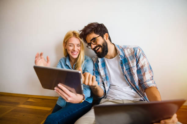istock Two young students sitting on a floor looking at the laptop. Laughing and gesturing with hands. 1041293360