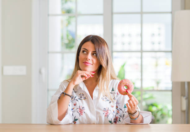 istock Young woman at home eating a doughnut serious face thinking about question, very confused idea 1041305018