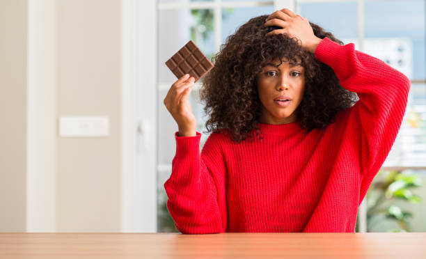 아프리카계 미국인 여자에 초콜릿 바 집 스트레스 수치와 충격 을된 머리에 손을 먹고 얼굴, 분노와 좌절을 놀라게. 두려워 하 고 실수에 대 한 화가. - confusion hand in hair tired touching 뉴스 사진 이미지