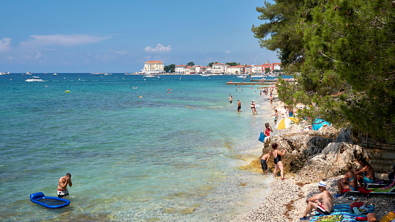 Porec, Croatia – July 22, 2018: bathing tourists on the beach of Porec in Croatia. In the background the old town.