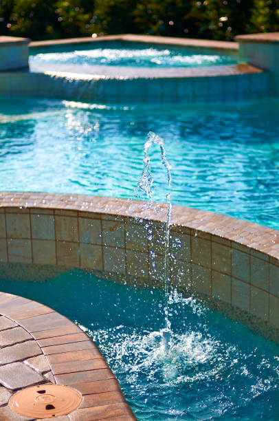 A Mini Fountain in a Clear Blue Pool with Tan Tiled Siding and a Corner Hot Tub stock photo