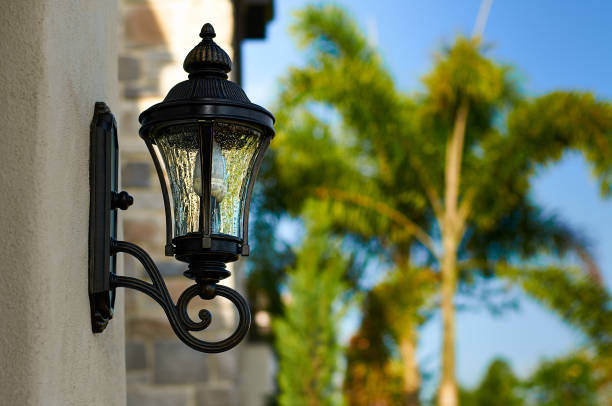 A Black, Curled, Outdoor Light Fixture on a Beige Wall with Palm Trees in the Background stock photo