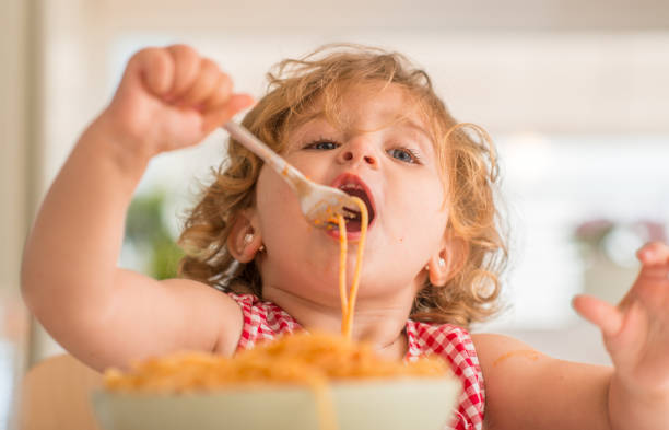 Little girl at home, beautiful toddler Beautiful blond child eating spaghetti with fork at home kids eating noodles stock pictures, royalty-free photos & images