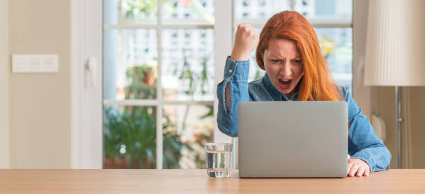 istock Redhead woman using computer laptop at home annoyed and frustrated shouting with anger, crazy and yelling with raised hand, anger concept 1041334098