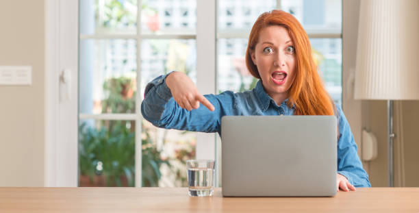 istock Redhead woman using computer laptop at home very happy pointing with hand and finger 1041334116