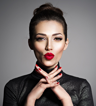 Closeup face of an young excited woman. Caucacian young adutl girl with a kiss gesture. Gorgeous female with red lipstick ona lips.