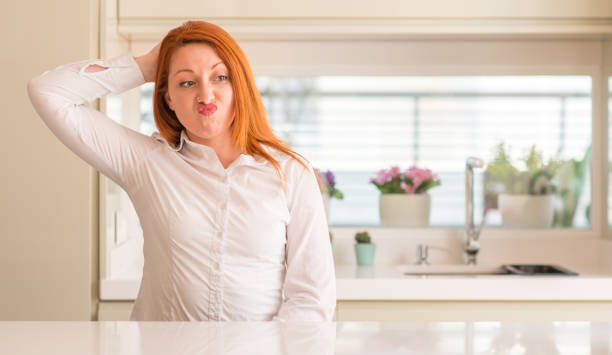 istock Redhead woman at kitchen confuse and wonder about question. Uncertain with doubt, thinking with hand on head. Pensive concept. 1041351952