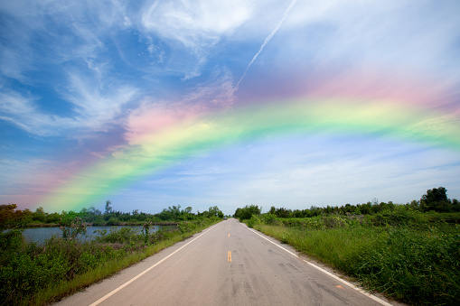 The Perspective line from road, grass on wayside and rainbow on the blue sky. never end to go concept. image for background, wallpaper and backdrop.
