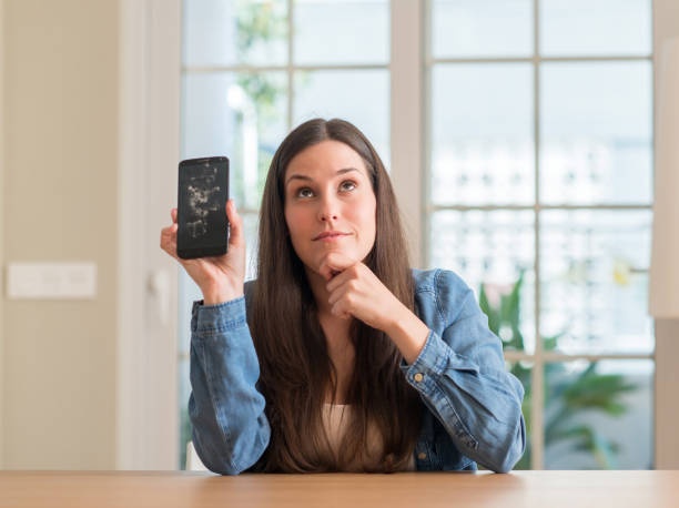 istock Brunette young woman holding broken smartphone serious face thinking about question, very confused idea 1041371342