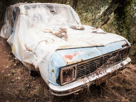 old abandoned car, left in the countryside, covered by a plastic sheet