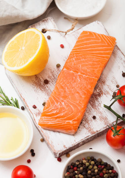 istock Fresh raw salmon slice on chopping board with oil tomatoes and lemon on stone kitchen table background. With rosemary and salt 1041407106
