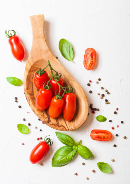 白いキッチンの背景に oilve 板でコショウとバジルつる有機ミニ サン マルツァーノ トマト - san marzano tomato ストックフォトと画像