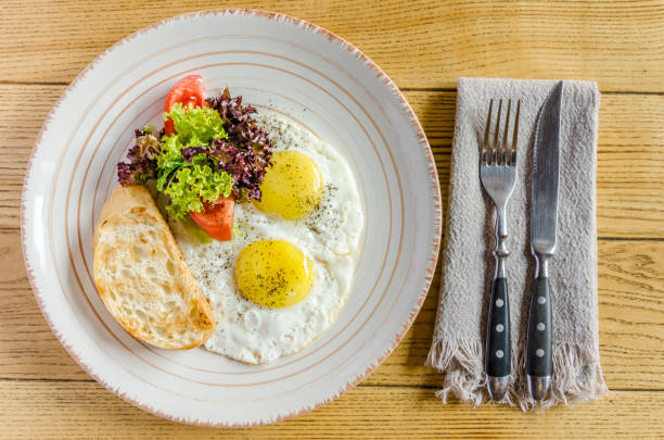 Healthy breakfast: Fried eggs, tomatoes, herbs and bread, with cutlery, on a wooden table. View from above