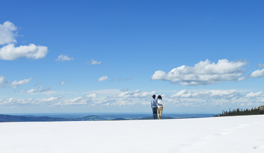 Young Asian couple hold each other, standing on snow at edge of Schafberg mountain (the mountain in movie 'sound of music'), Austria