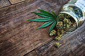 Cannabis bud pouring out of a glass jar on wood background