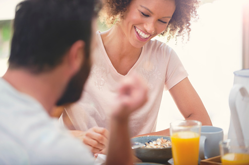 Happy couple having breakfast together. She is African American and has an afro. He has a beard. They are having muesli, orange juice and coffee. They are smiling and laughing and having fun