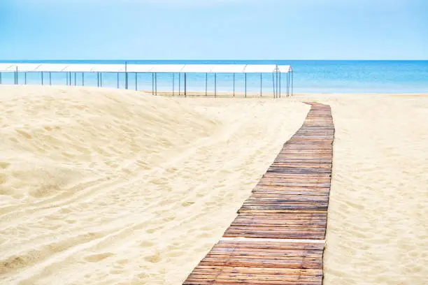 Panoramic view of a deserted sandy beach with wooden pathway in Anapa, Russia. Beautiful beach on the Black Sea for background. Tourist track with decking on the beach. Concept of summer vacation.