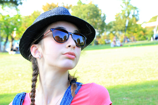 Portrait of young beautiful teenage girl wearing hat and sunglasses in the park
