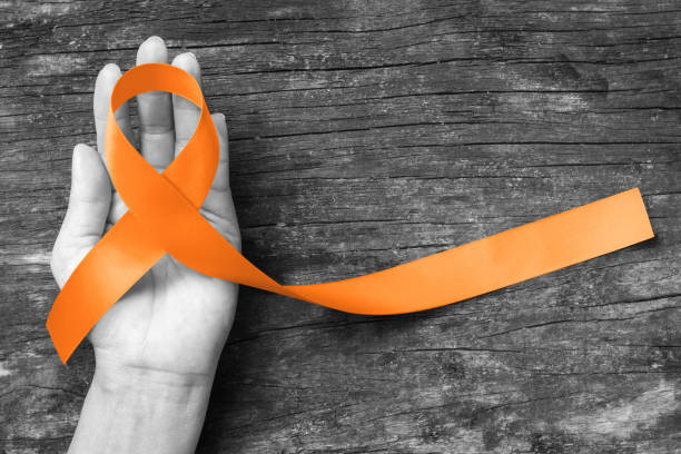Orange ribbon for Leukemia, Kidney cancer, RDS multiple sclerosis awareness on human hand, aged background; Satin fabric color symbolic concept for raising public support on people living with disease Orange ribbon for Leukemia, Kidney cancer, RDS multiple sclerosis awareness on human hand, aged background; Satin fabric color symbolic concept for raising public support on people living with disease self harm photos stock pictures, royalty-free photos & images