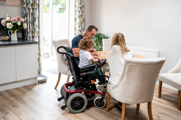 Boy in wheelchair doing jigsaw with parents 6 year old boy with muscular dystrophy, sitting at dining table with mother and father, playing a game, quality time with family family playing card game stock pictures, royalty-free photos & images