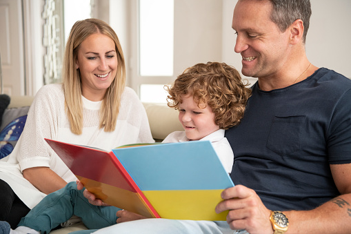 6 year old boy with muscular dystrophy, sitting on couch, looking at book with mother and father