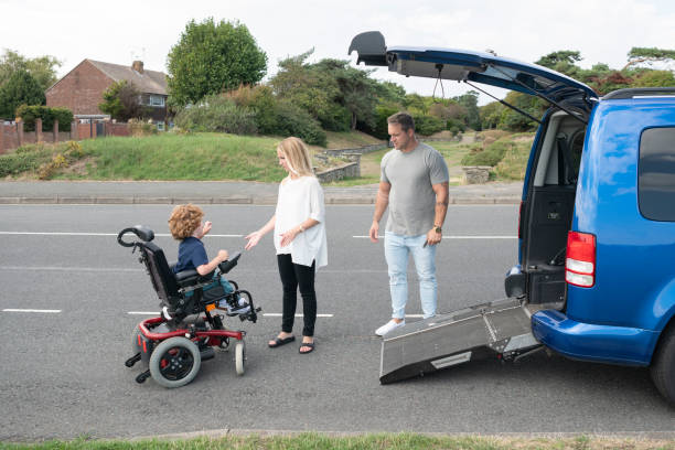 Young boy operating wheelchair to access car ramp 6 year old child with muscular dystrophy steering his electric wheelchair to gain access to family car, mother and father assisting and encouraging northern europe family car stock pictures, royalty-free photos & images