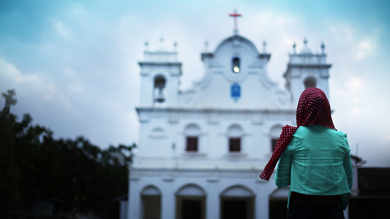 Young Christian woman standing in front of holy church and she praying to God, Goa/India.