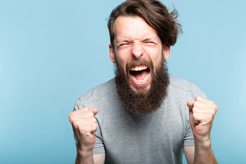 anger and fury. emotional or mental breakdown. enraged man screaming. portrait of a young bearded guy on blue background. facial expression and feelings concept.