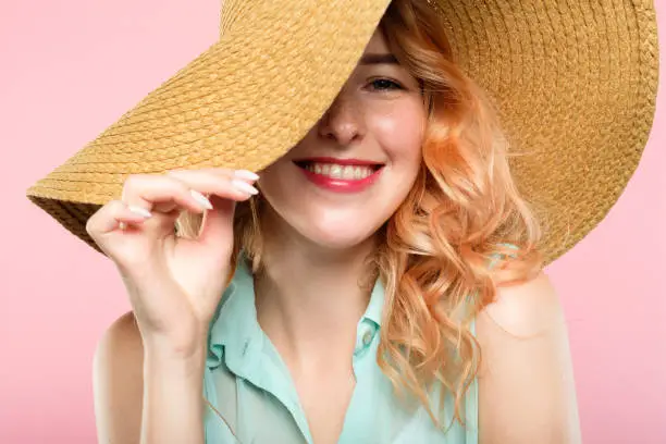 emotion expression. smiling happy woman pleased with herself. self-satisfied young beautiful girl in a sunhat. summer beauty and fashion concept. portrait on pink background.