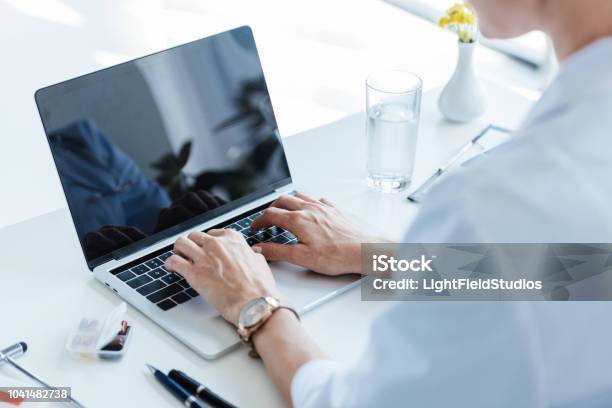 Partial View Of Female Doctor Typing On Laptop With Blank Screen At Table In Office Stock Photo - Download Image Now