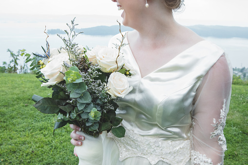 An unrecognizable bride stands on a scenic bluff outdoors.  She turns to look behind her as she laughs.