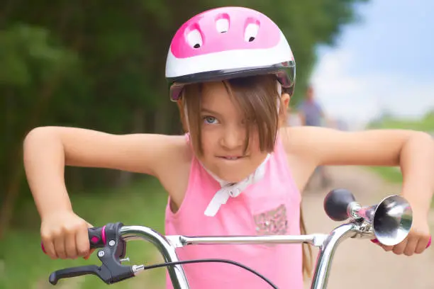 Photo of Portrait of a little girl in a pink safety helmet driving her bike.