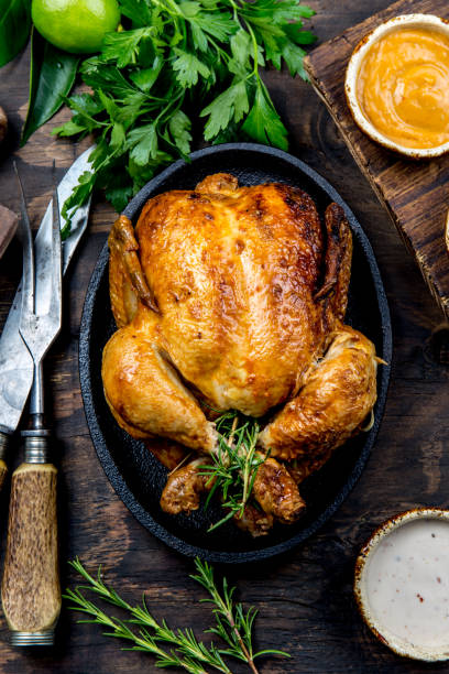 Roasted chicken with rosemary served on black plate with sauces on wooden table, top view. stock photo