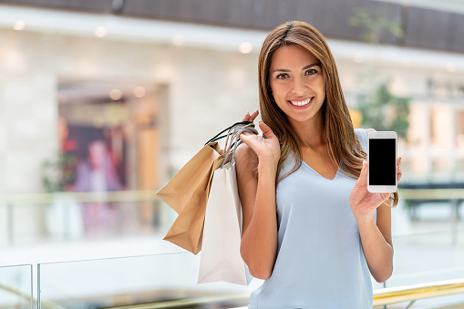 Portrait of a very happy shopping woman using her cell phone and showing the screen towards the camera