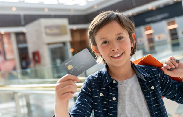 happy boy shopping at the mall and holding a credit card - paying children only retail childhood imagens e fotografias de stock