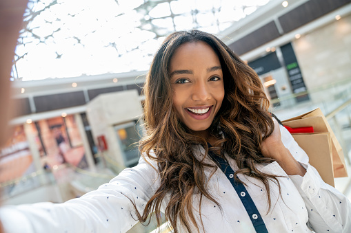 Portrait of a happy shopping woman taking a selfie at the mall and looking at the camera smiling