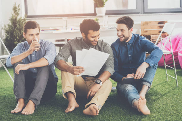 istock Smiling young barefoot businessmen sitting with papers and using digital tablet, business teamwork concept 1041494366