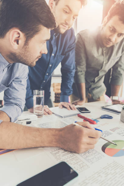 istock Three young businessmen leaning at table and working at project together, business teamwork concept 1041494406