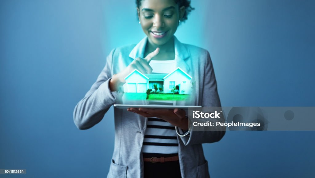 Your perfect home is just an app away Studio shot of a young businesswoman using a digital tablet with property graphics against a blue background Real Estate Stock Photo