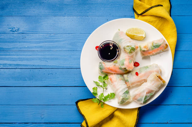 istock Vegetarian spring rolls with tofu, marinated carrot and daikon and cilantro on blue painted wooden table with yellow textile 1041513928