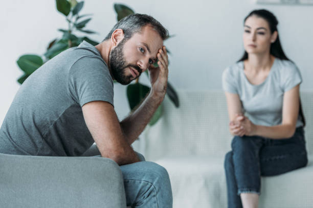 istock upset middle aged man sitting on couch and girlfriend sitting behind 1041514416