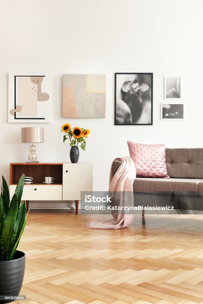 Gallery in white living room interior with sofa with pink pillow and coverlet, sunflowers on cupboard and herringbone floor in the real photo Herringbone Stock Photo