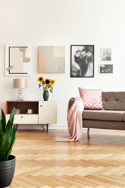 galeria w białym salonie wnętrze z sofą z różową poduszką i okładką, słoneczniki na szafce i jodełkę podłogi na prawdziwym zdjęciu - herringbone zdjęcia i obrazy z banku zdjęć