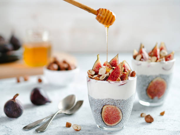 chia pudding with yogurt, figs, nuts, honey Healthy chia pudding with yogurt, figs and nuts in glass. Ideas and recipes for healthy breakfast, snack or dessert. Honey drips into glass with chia seeds pudding. Copy space for text. fig photos stock pictures, royalty-free photos & images