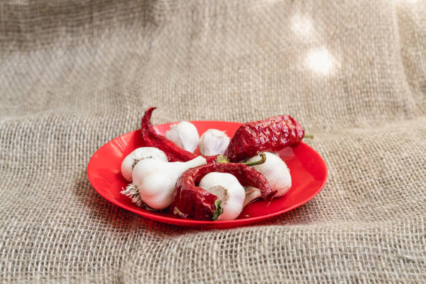 White garlic with red peppers on a red plate. Flat lay with textile background