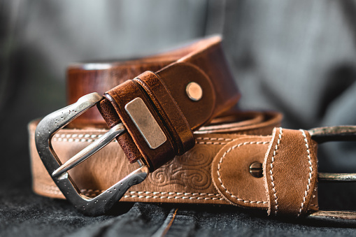 Two brown leather belts on dark background. Front view