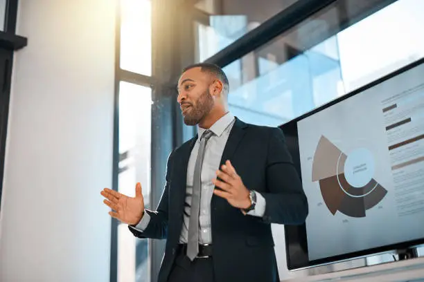 Shot of a young businessman presenting data on a screen during a meeting in an office