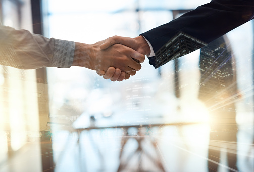 Closeup shot of businesspeople shaking hands in an office superimposed over a cityscape