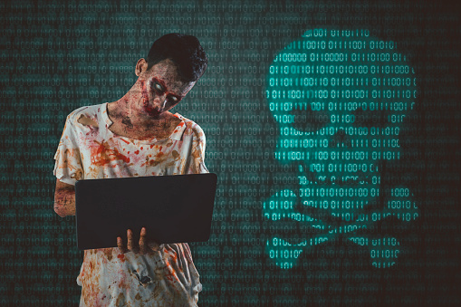 Picture of male zombie using a laptop while standing with danger symbol in code binary background